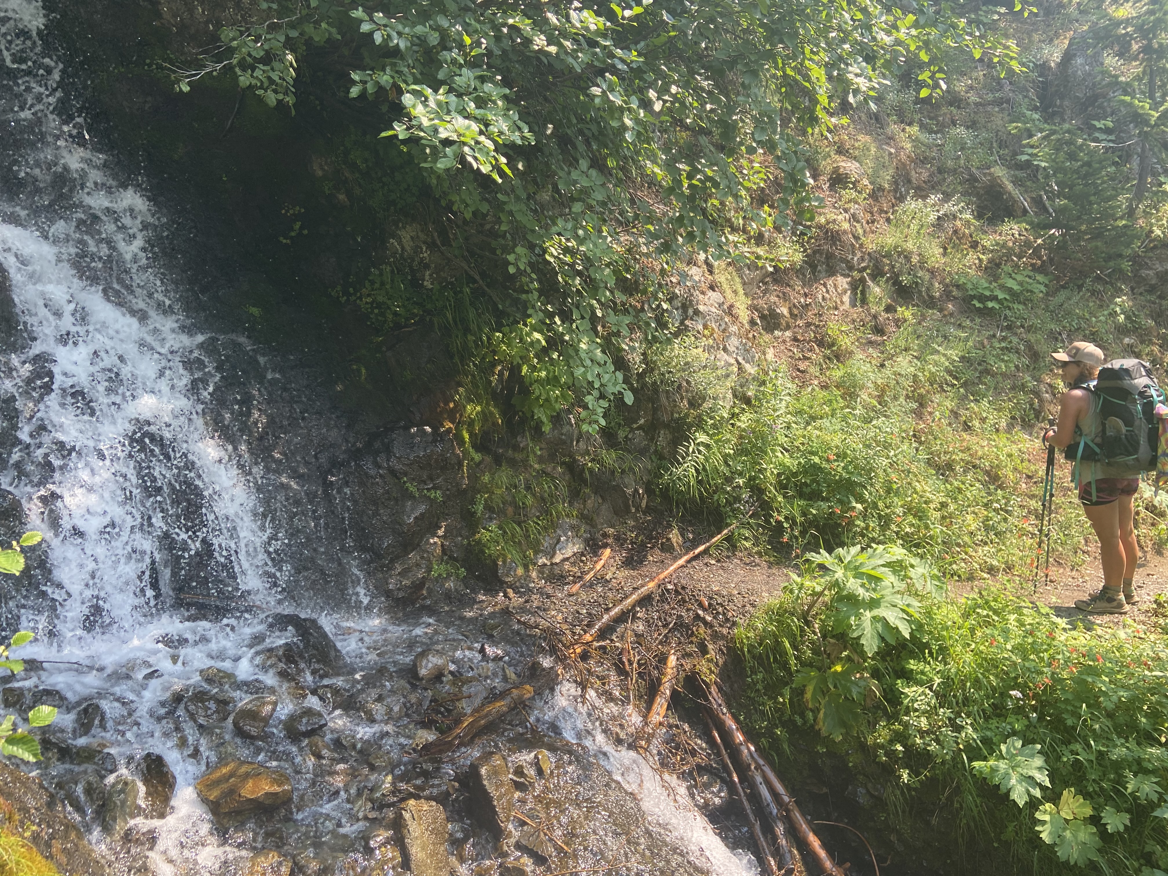A woman standing by a waterfall that crosses the trail.