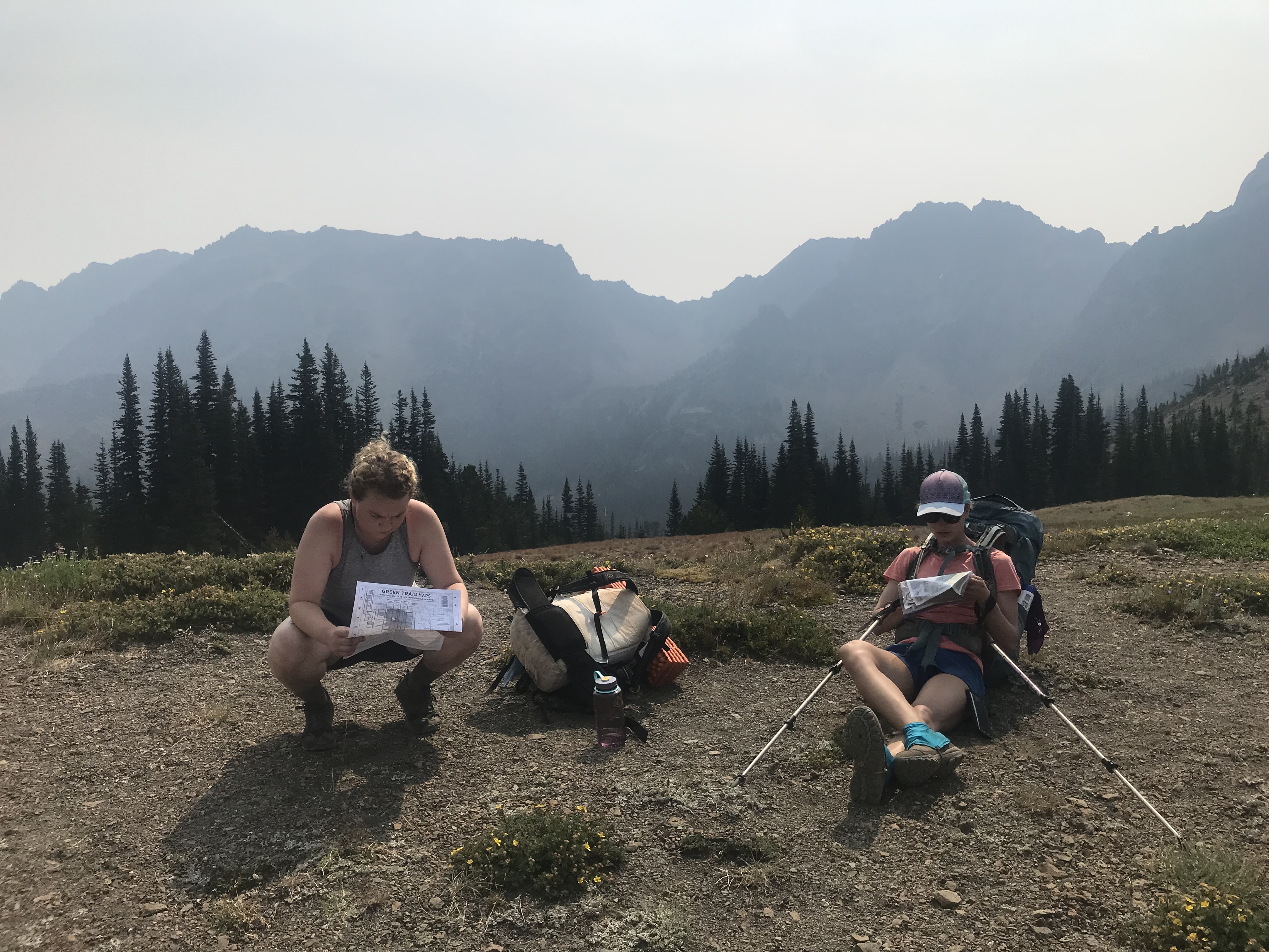 Two women sitting side-by-side reading maps.