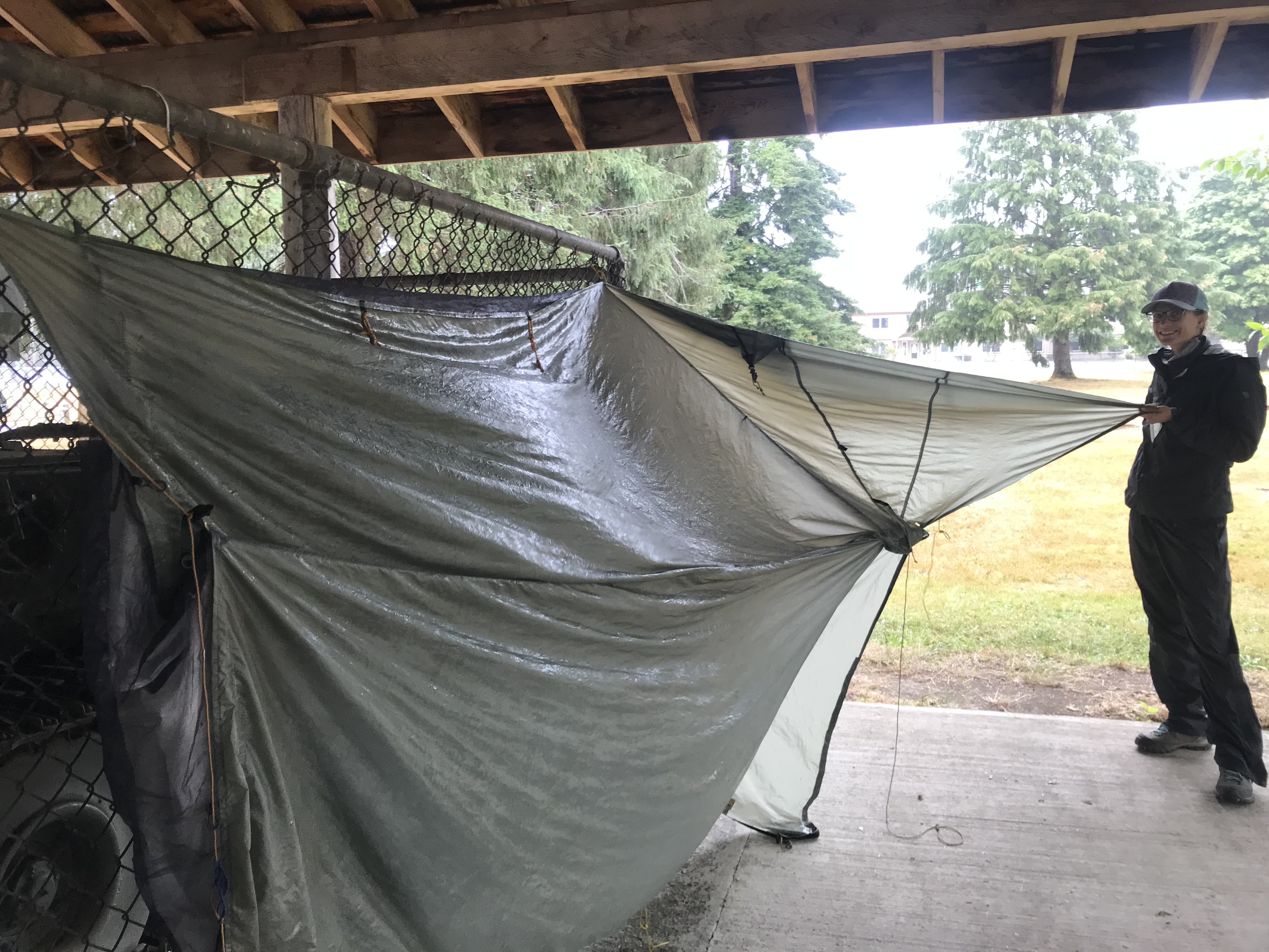 Woman in raingear trying to dry a wet tent in a park pavilion.