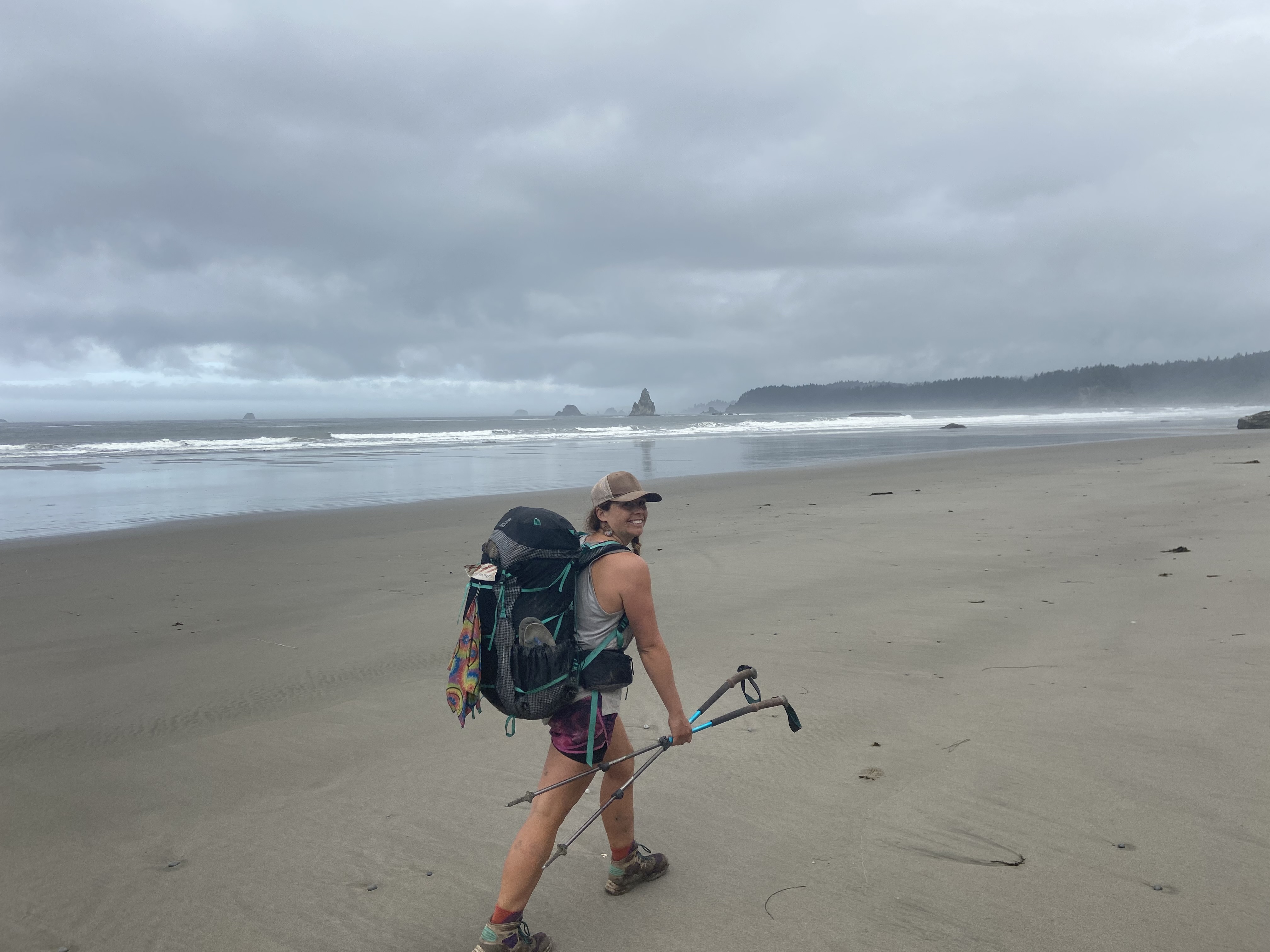 A woman walking on the beach and wearing a backpack.