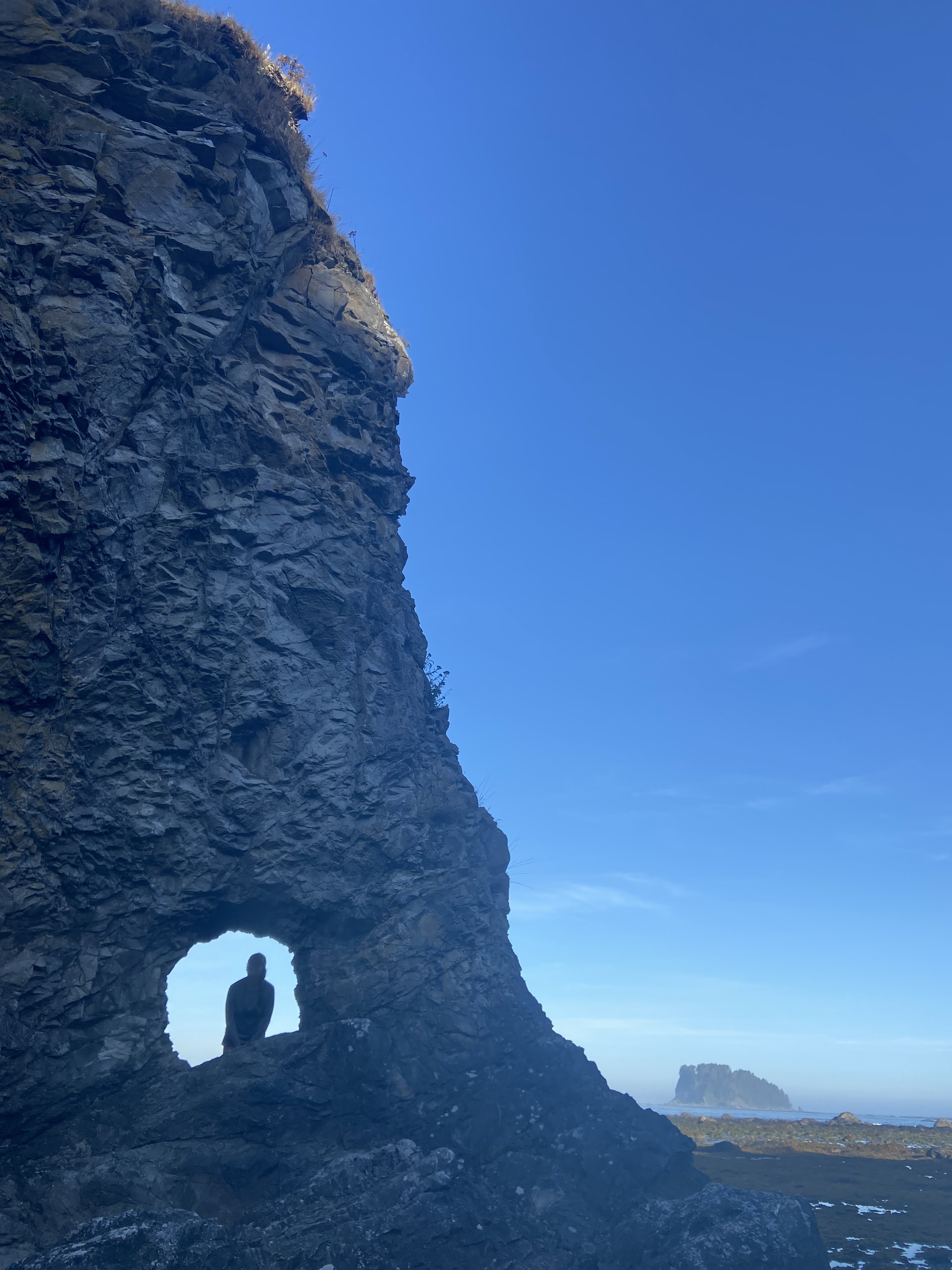 A person's silhouette through a hole in the rock along the shore.
