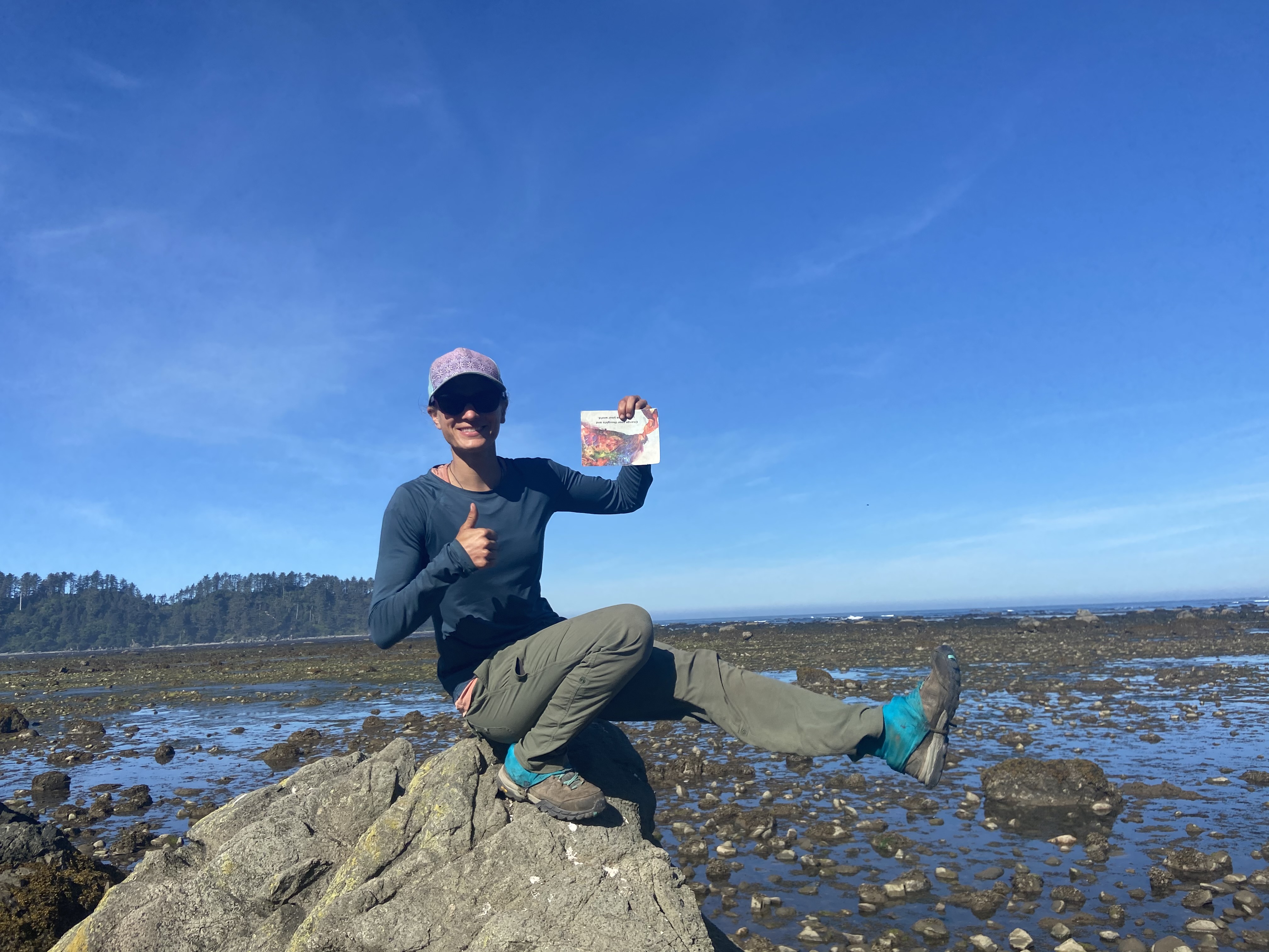 A person doing a one-legged squat on a rock by the shore, holding a postcard that says "Change your thoughts, change your world."