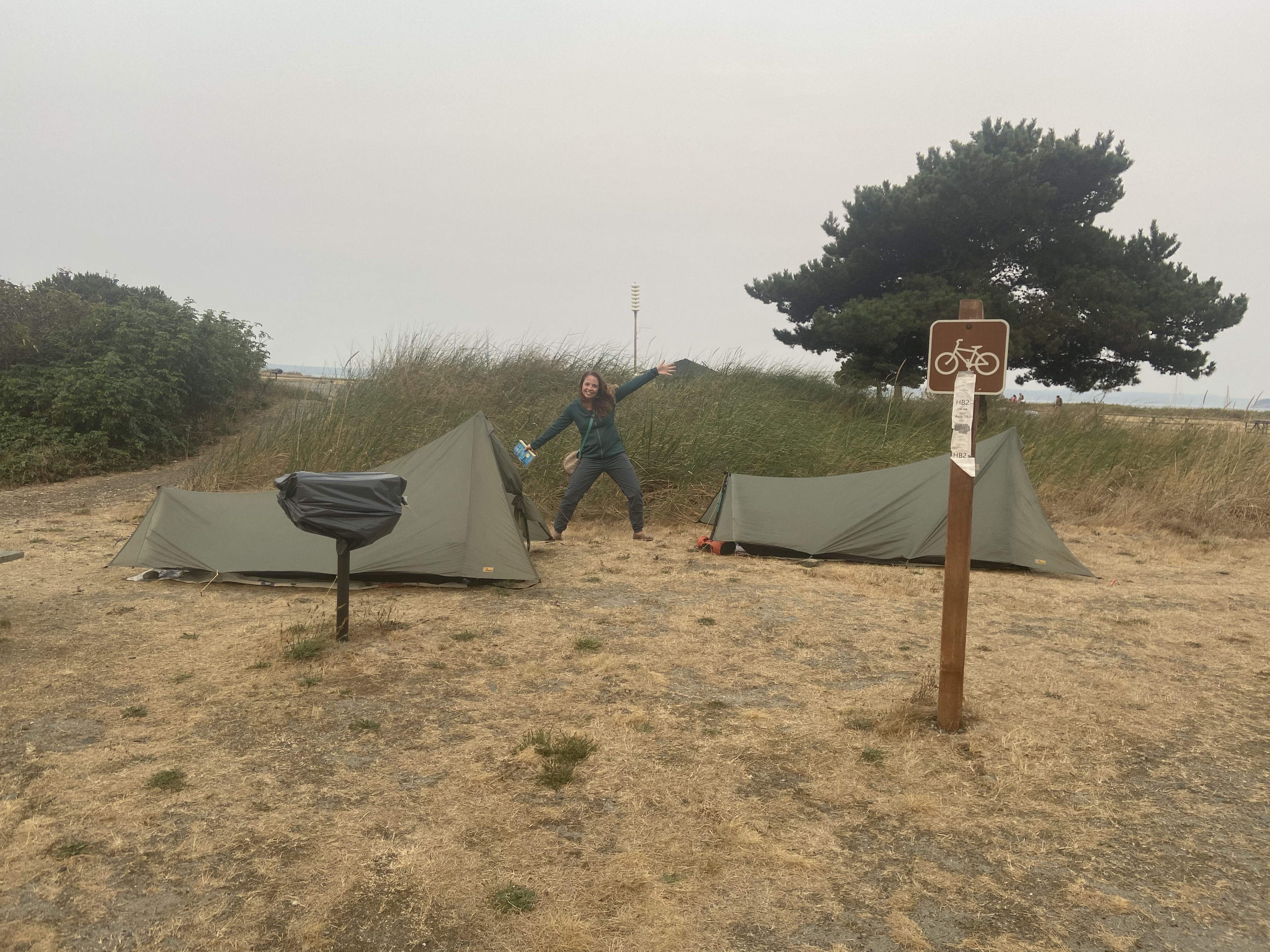 A person between two tents in a campground striking a pose.
