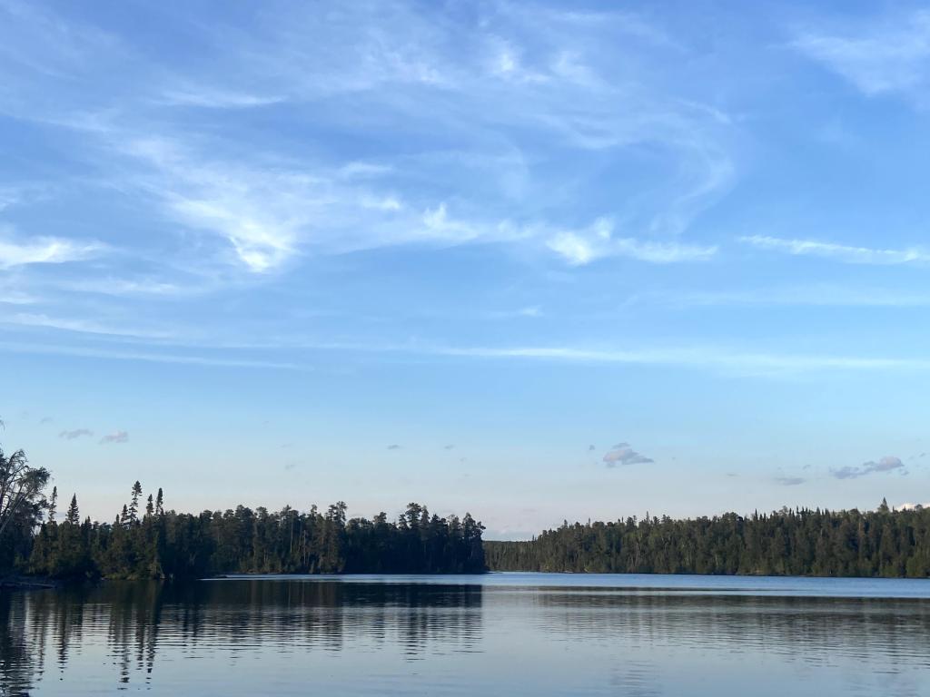 A sunset on a lake with wispy white clouds.