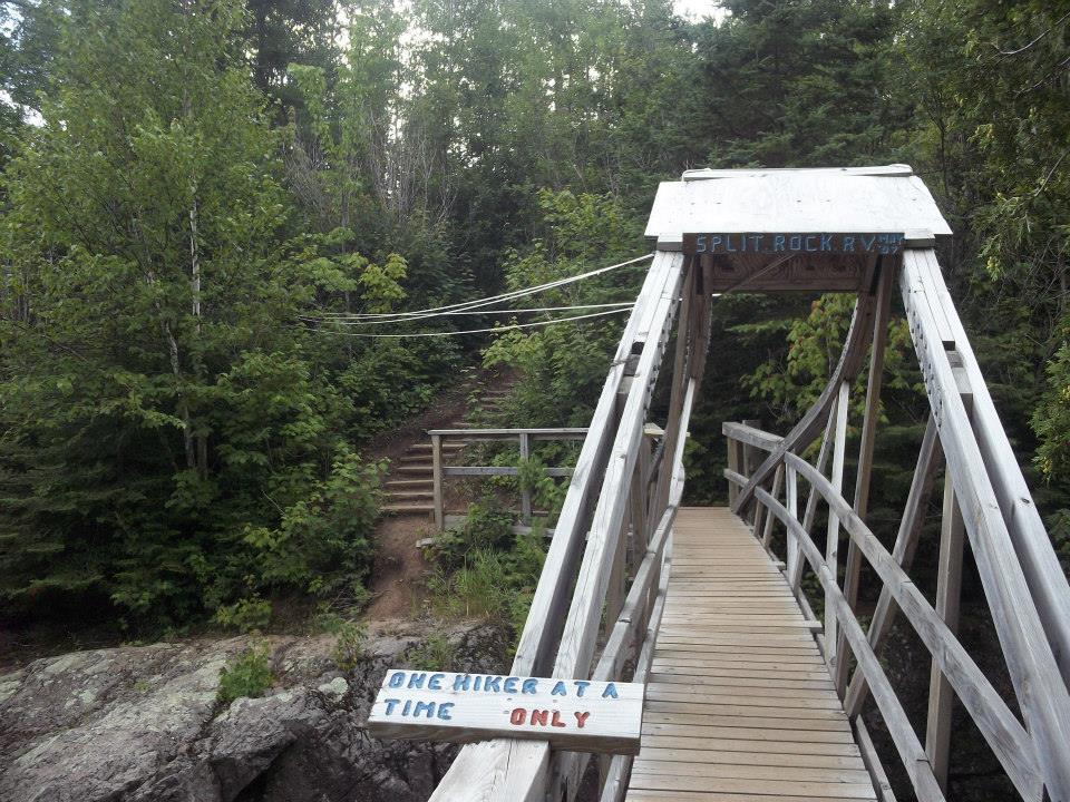 A bridge over the Split Rock River that is listing heavily to one side. There is a sign that says "one hiker at a time only" on it.