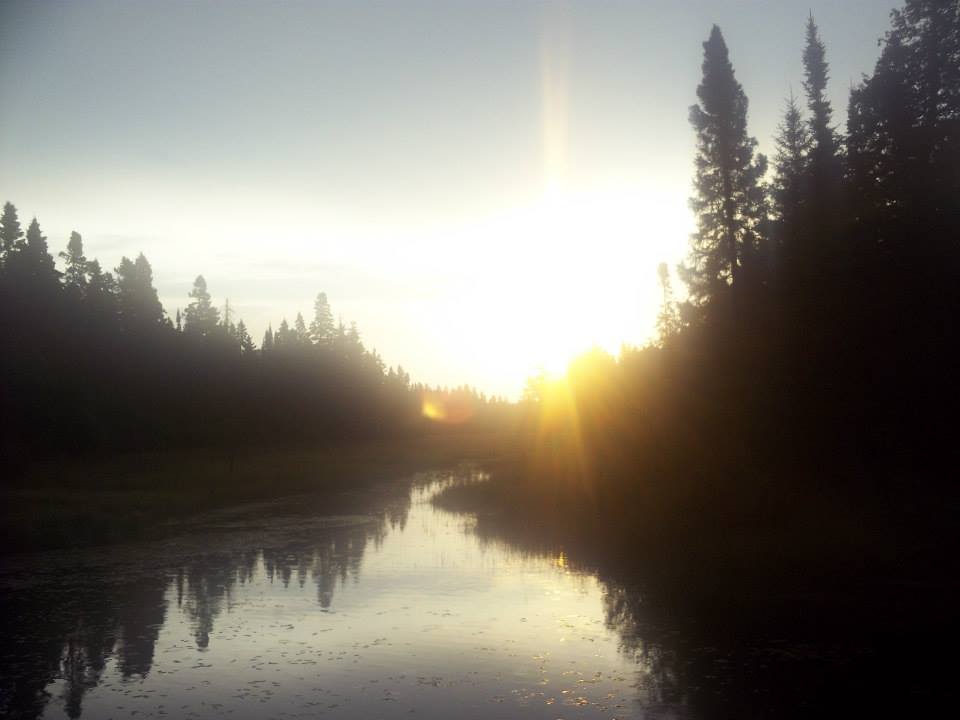 A blurry picture of a pond with the sun low on the horizon. There are water droplets on the lens.