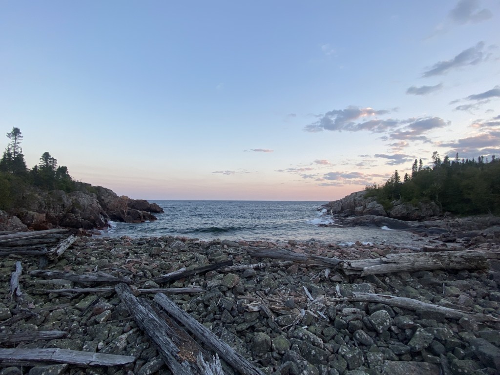 A view looking out from a rocky beach, with the sky showing evening colors and a few clouds.