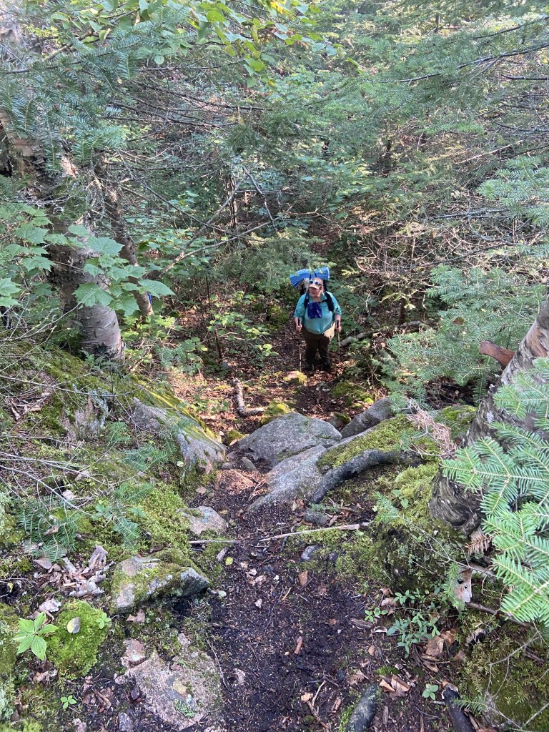 A woman with a backpack at the bottom of a steep, rocky climb.