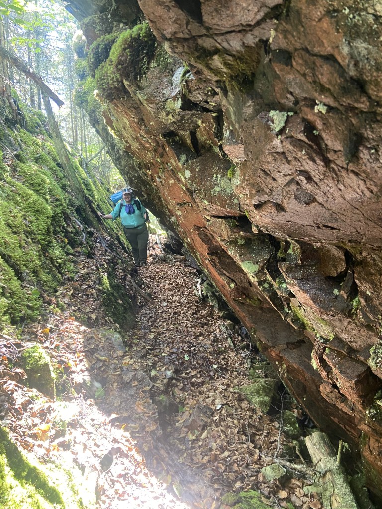 A slanty crack in the rock, with a woman at one end to show scale (the crack is as big as she is, and the trail travels through it).